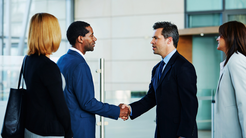 Two business men shaking hands with others surrounding them